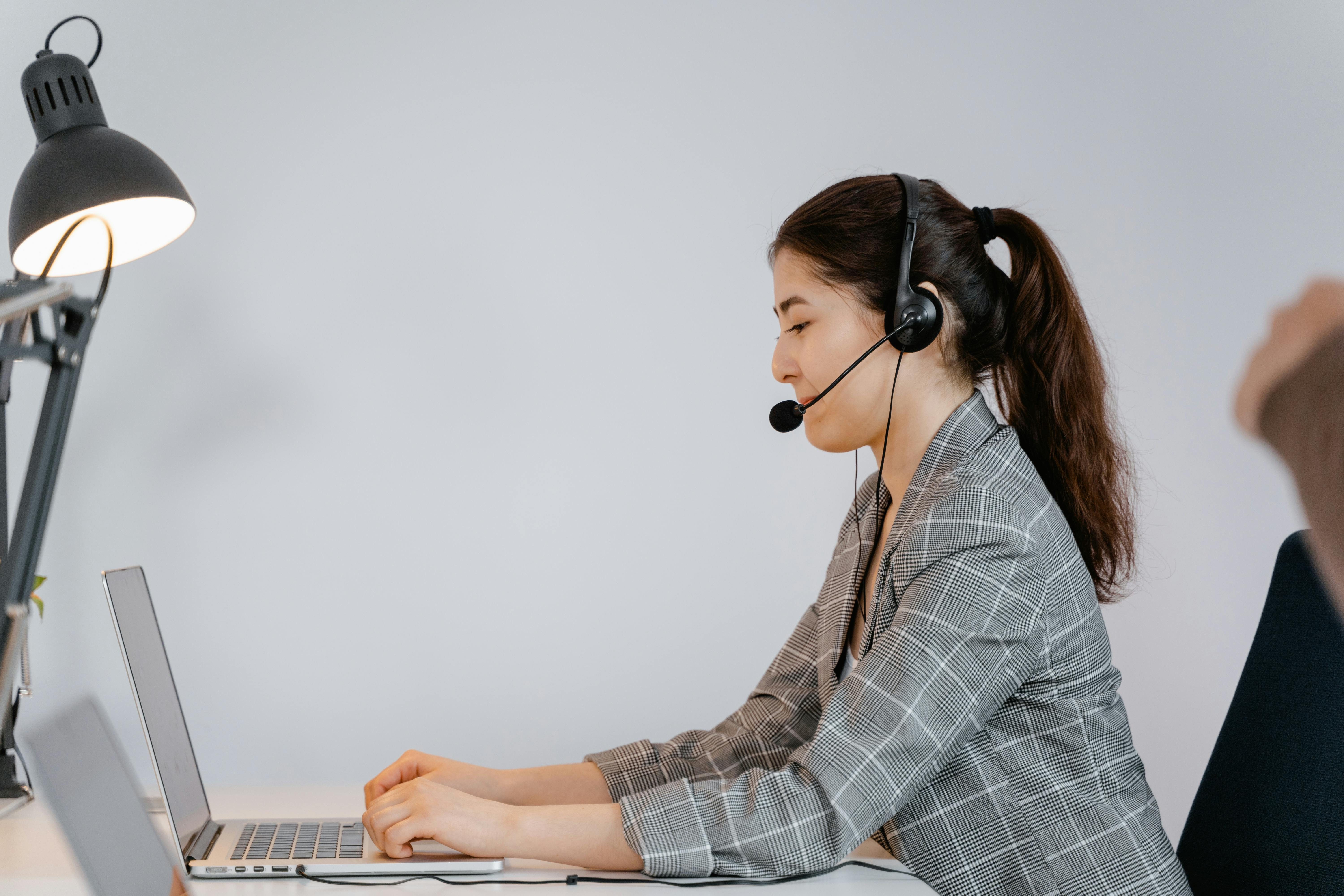 Asian woman working in customer support at office with headset and laptop